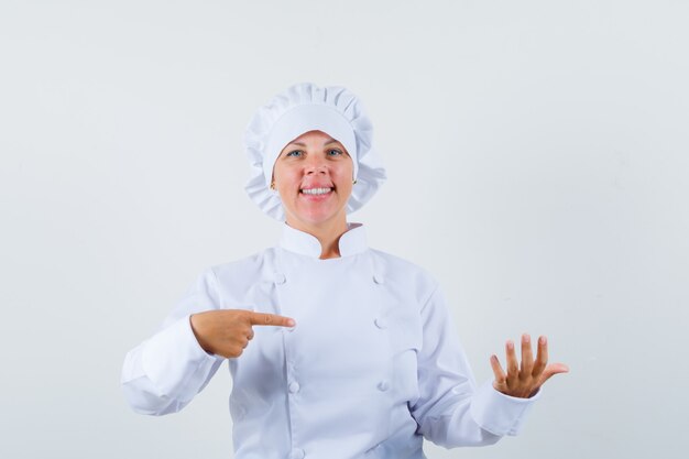 woman chef pointing at something pretended to be held in white uniform and looking confident