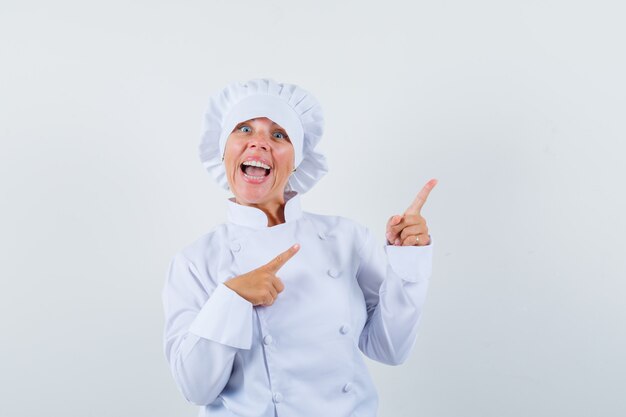 woman chef pointing at upper right corner in white uniform and looking frisky.