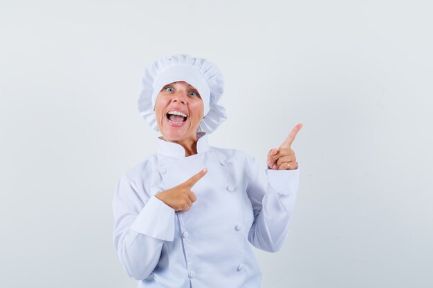 женщина-повар, указывая на верхний правый угол в белой форме и выглядя резво.