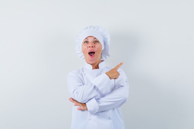 woman chef pointing at upper right corner in white uniform and looking joyful.