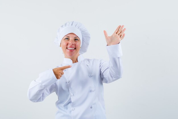 woman chef posing like pointing at her hand holding phone in white uniform and looking concentrated.