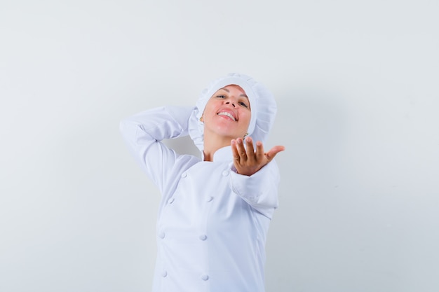 Chef donna in posa mentre allunga la mano in uniforme bianca e sembra carina.