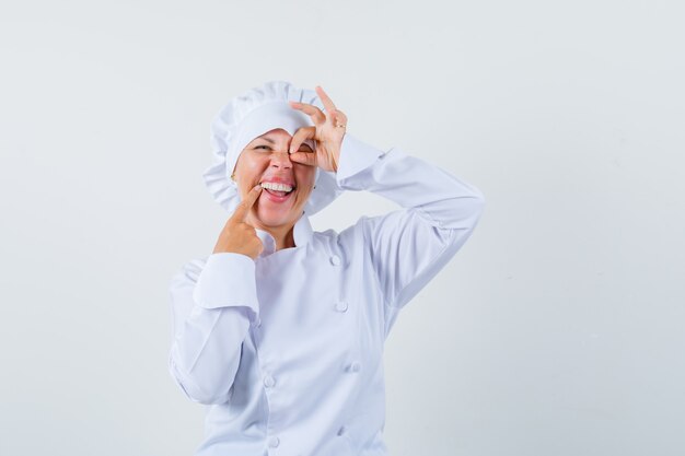 woman chef showing ok sign on eye in white uniform and looking optimistic.