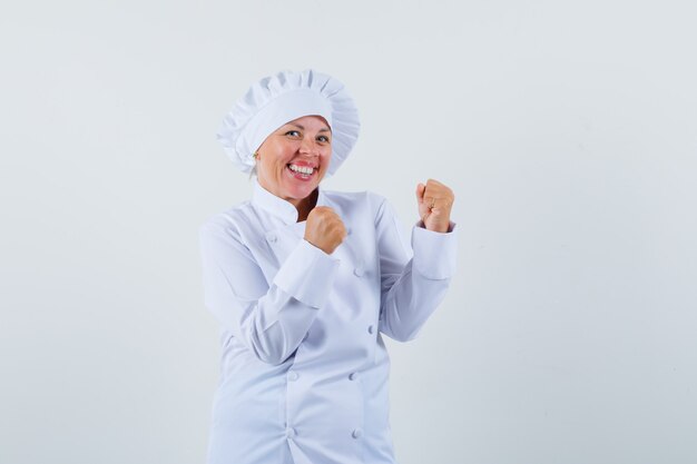 흰색 유니폼에 승자 제스처를 보여주는 쾌활한 찾고 여자 요리사