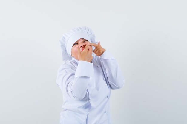 woman chef squeezing her pimple on cheek in white uniform