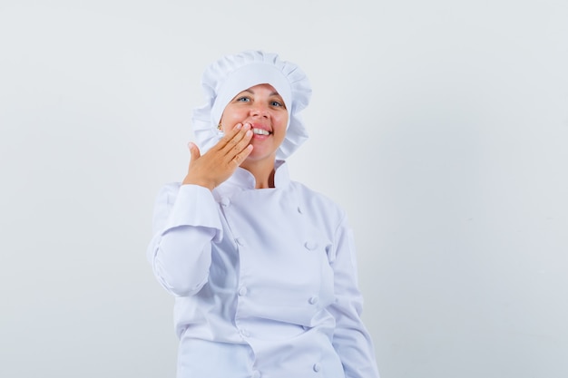 woman chef in white uniform holding hand near mouth and looking cheery