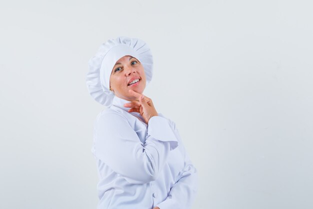 woman chef in white uniform touching her chin with finger and looking charming