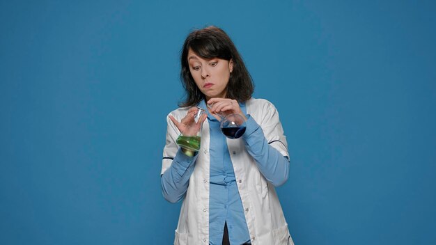 Woman chemist analyzing genetic substance in lab beakers, wearing white coat. Biochemistry specialist wokring with liquid sample in flask or jar to do pharmaceutical research in studio.