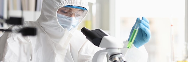 Woman chemist in protective suit conducts laboratory research on green liquid discovery of new