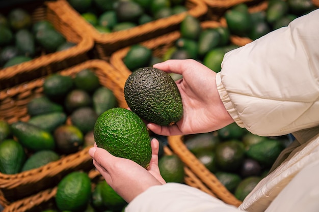 A woman chooses an avocado in a grocery store