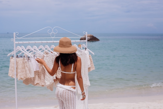 Woman choosing knitted clothes from hangers on the beach