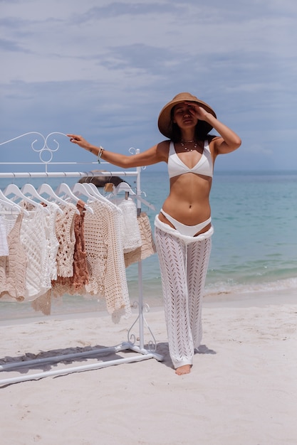 Woman choosing knitted clothes from hangers on the beach