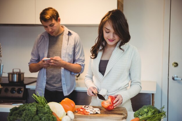 Woman chopping vegetables and man using mobile phone in the kitchen