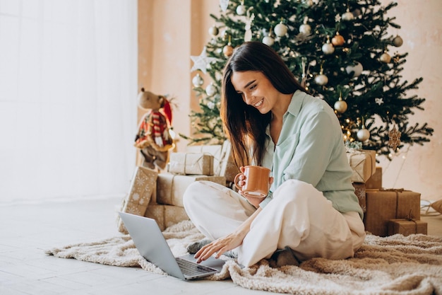 Женщина на Рождество с ноутбуком и пьет чай у елки