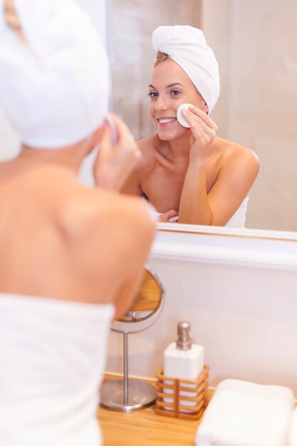 Woman cleaning face in front of mirror