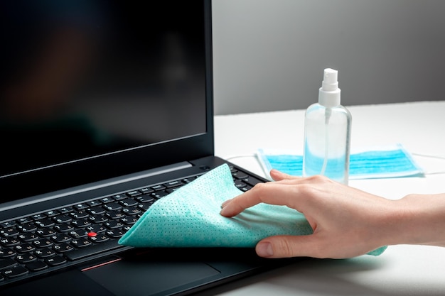 Woman cleaning keyboard. new normal cleaning laptop work home surfaces. female hands disinfecting laptop keyboard using disinfectant spray, alcohol sanitizer, wet disinfectant wipes.