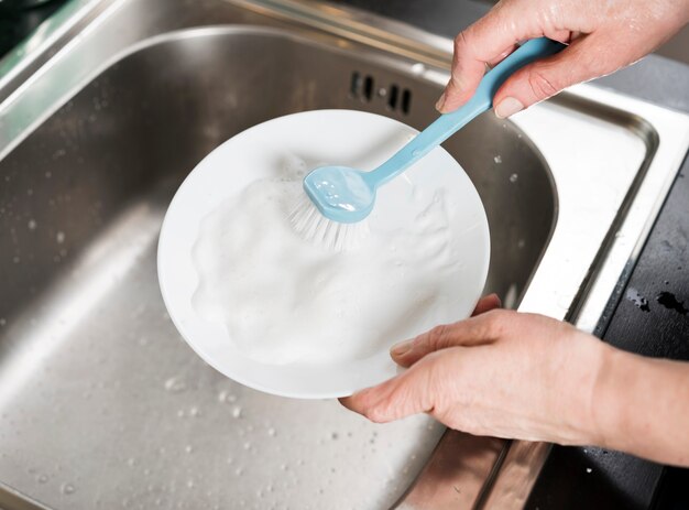 Женщина чистит тарелку в раковине с кисточкой