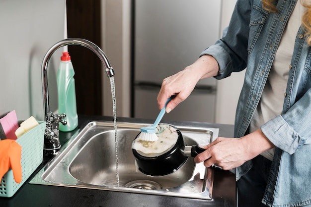 Woman cleaning a pot in the sink with brush