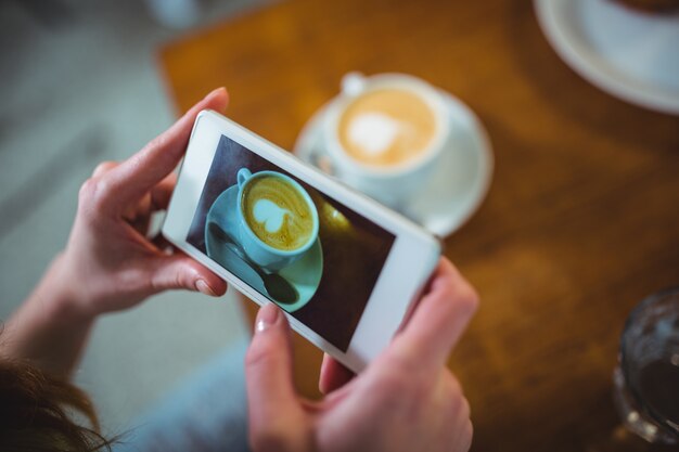 携帯電話からのコーヒーの写真をクリックする女