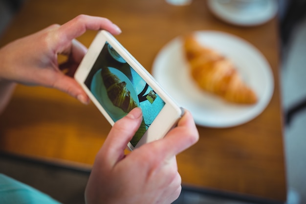 Woman clicking photo of croissant from mobile phone