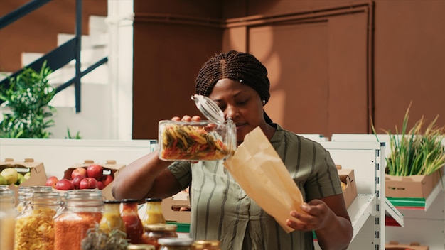 Free photo woman client filling in paper bag with pasta sold as bulk item