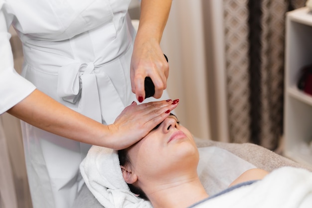 Woman client in salon receiving manual facial massage from beautician