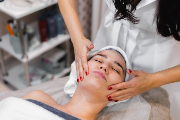 Woman client in salon receiving manual facial massage from beautician