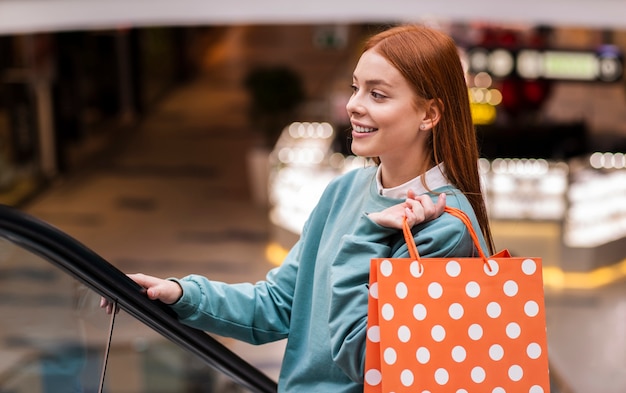 Free photo woman climbing escalator and holding paper bag