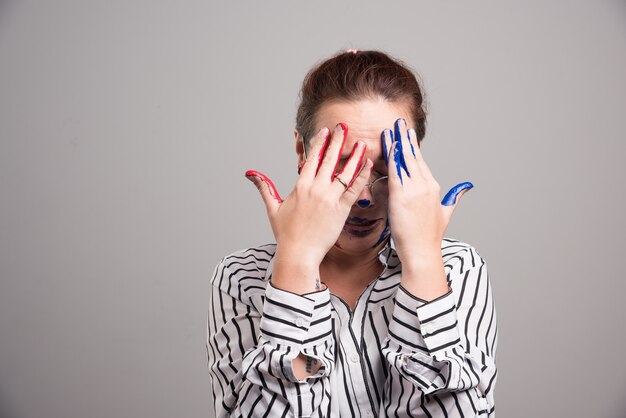 Woman closed her face with paints hands on gray background