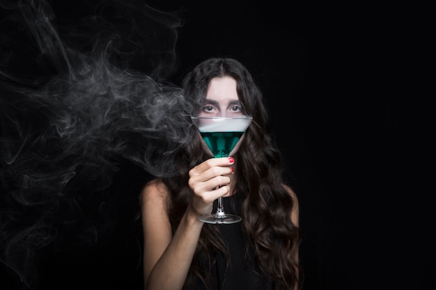 Free photo woman closing face by goblet with smoking turquoise liquid