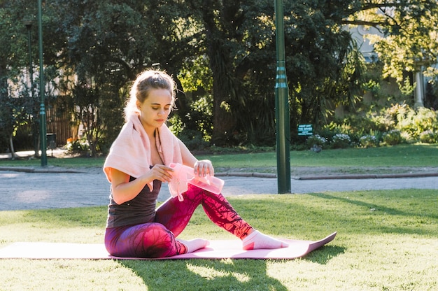 Foto gratuita donna che chiude la bottiglia d'acqua sulla stuoia di stretching