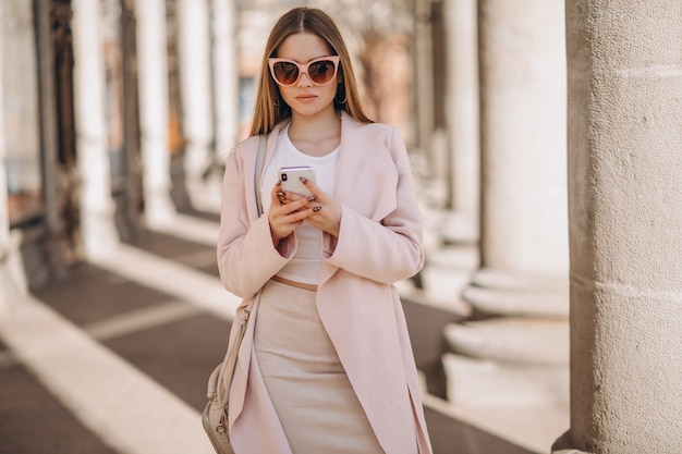 Женщина в пальто гуляет на улице и разговаривает по телефону