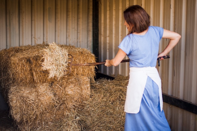 Free photo woman collecting hay with pitchfork