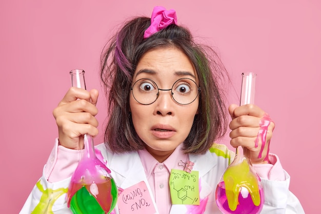 無料写真 医療用白衣を着た女性が科学研究を行い、実験結果に驚いた色とりどりの液体が入ったガラス製ビーカーをピンク色の眼鏡をかけている