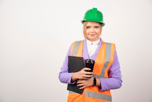 woman contractor in hard hat with clipboard and black cup on white.