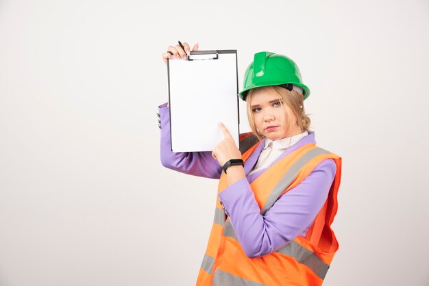 woman contractor with green helmet holding clipboard on white.