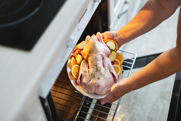 Woman cooking christmas duck puting raw duck with vegetables in oven.