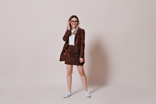 woman in corduroy suit and glasses posing on beige wall