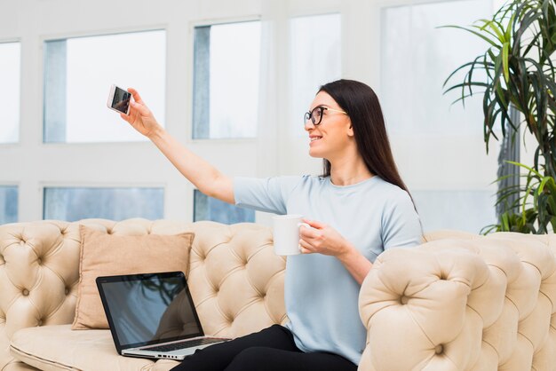 Woman on couch taking selfie with coffee 