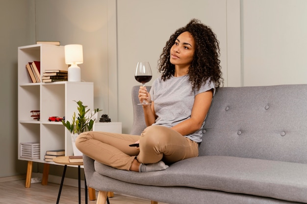 Женщина на диване смотрит телевизор и пьет вино