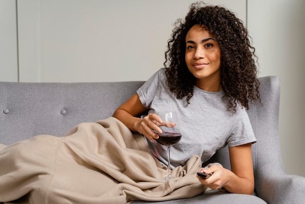 Donna sul divano a guardare la tv e bere vino