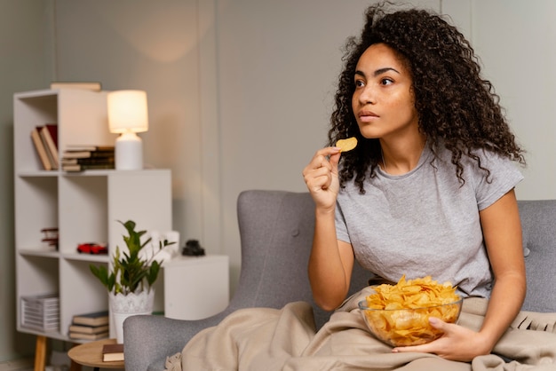 Donna sul divano a guardare la tv e mangiare patatine