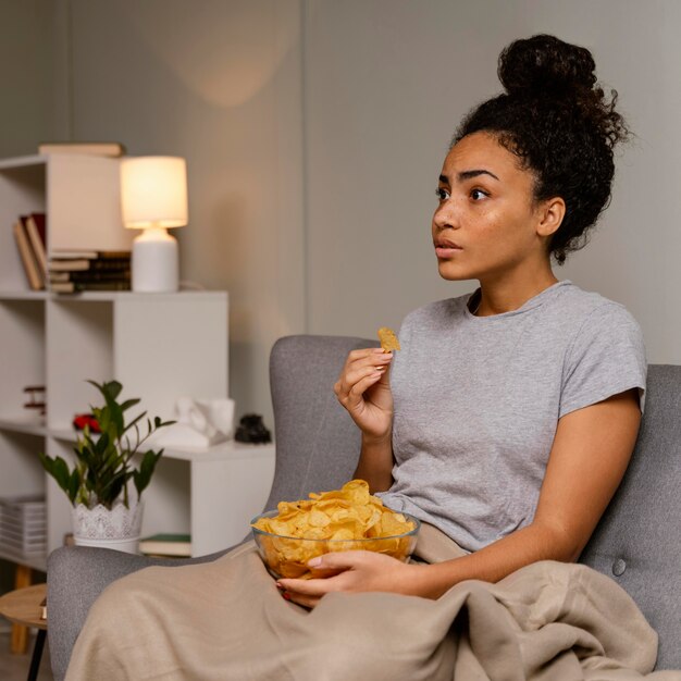 Woman on couch watching tv and eating chips