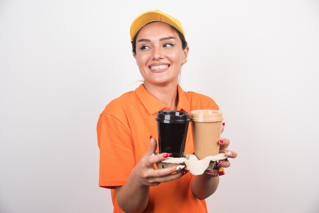 Woman courier holding two cups of coffees laughing.