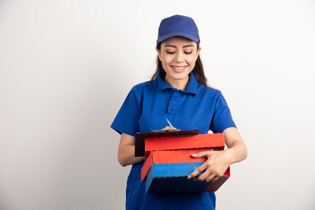 Woman courier writing in clipboard and holding cardboards of pizza