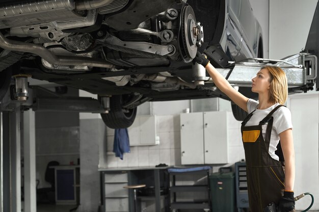 Woman in coveralls fixing brake discs of lifted car.