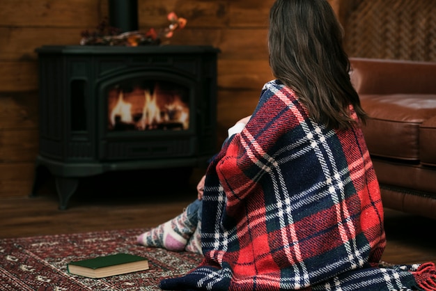 Woman covered in blanket next to fireplace
