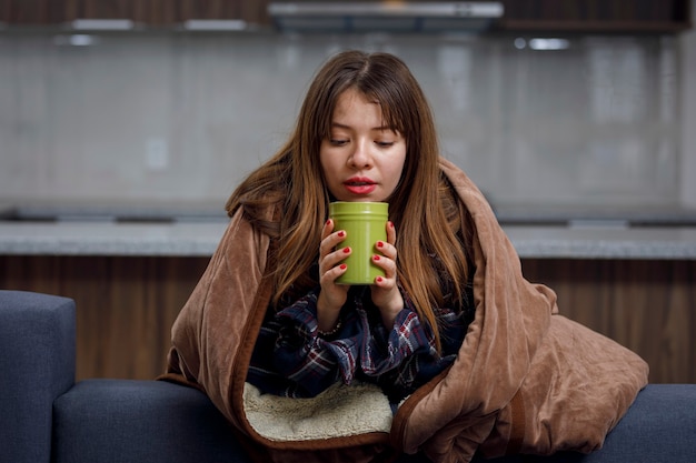 집에서 커피를 마시는 동안 담요로 덮인 여성