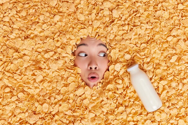 woman covered with cornflakes bottle of fresh milk feels excited has scared shocked expression