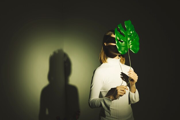 Woman covering face with big green leaf 